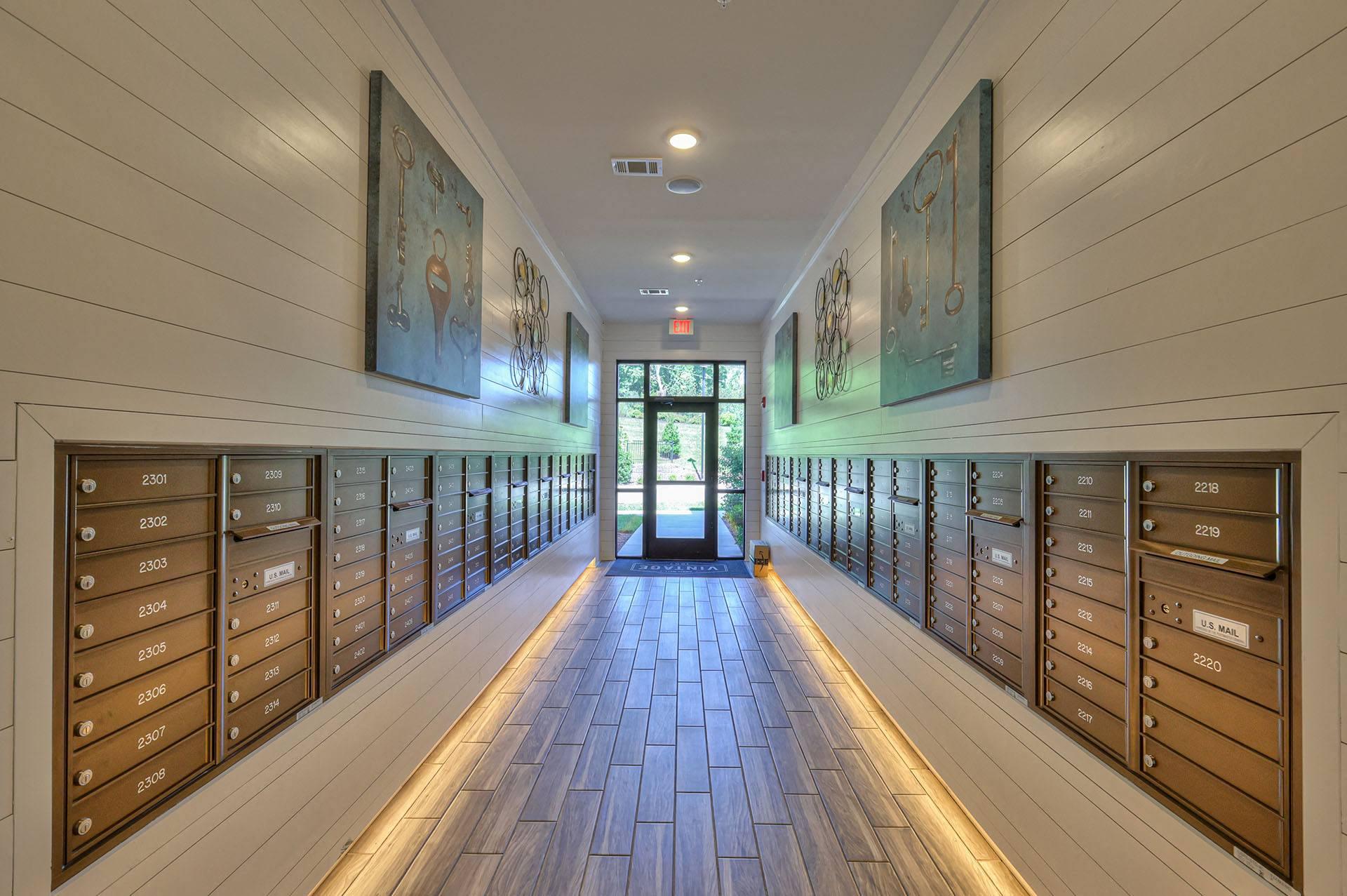 A hallway with a series of mailboxes on the wall and a door at the end.