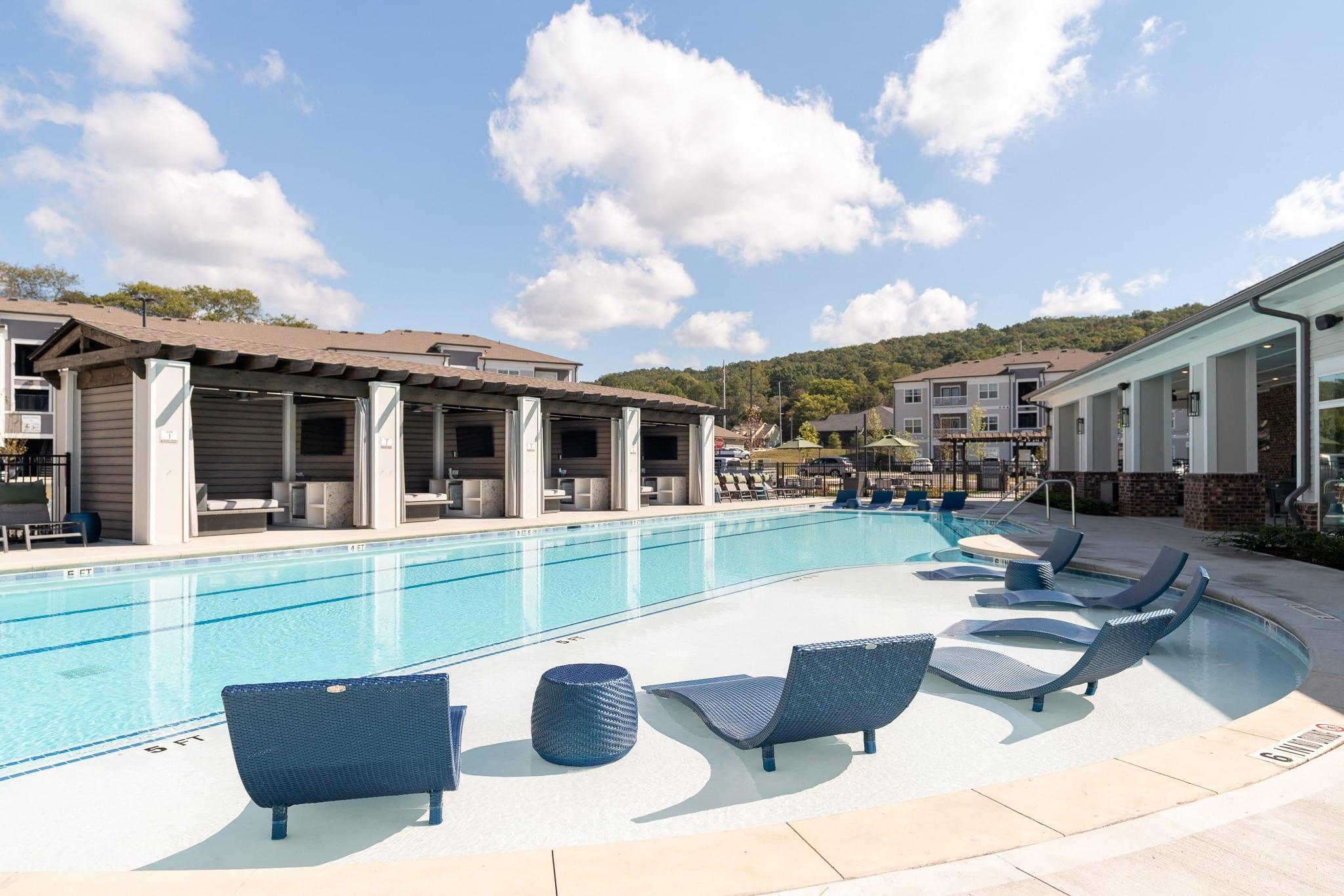 A pool with sun loungers and a building in the background.