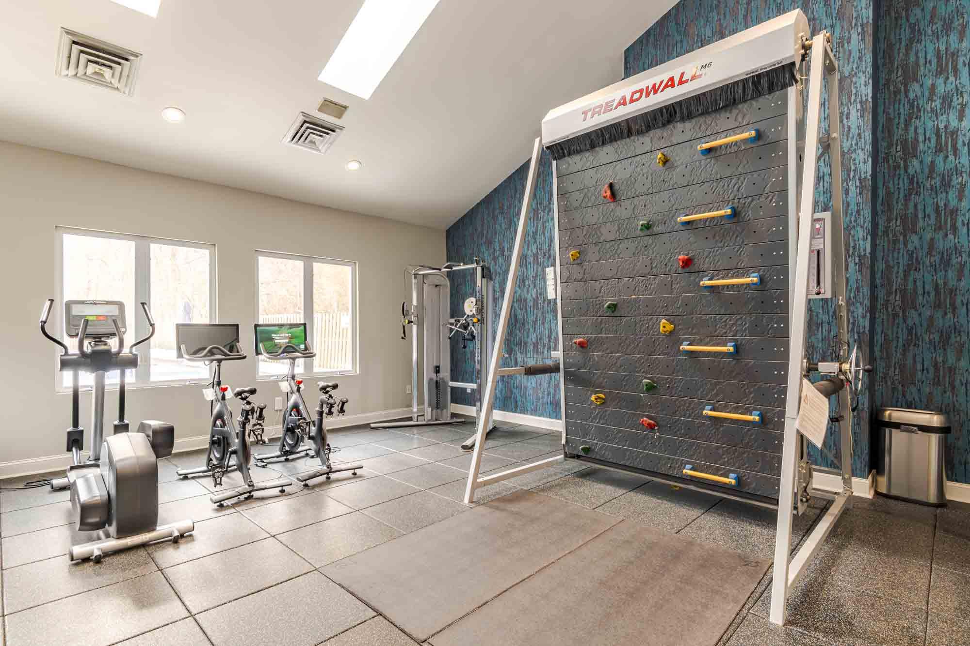 A room with a wall-mounted climbing wall, exercise bikes, and a treadmill.