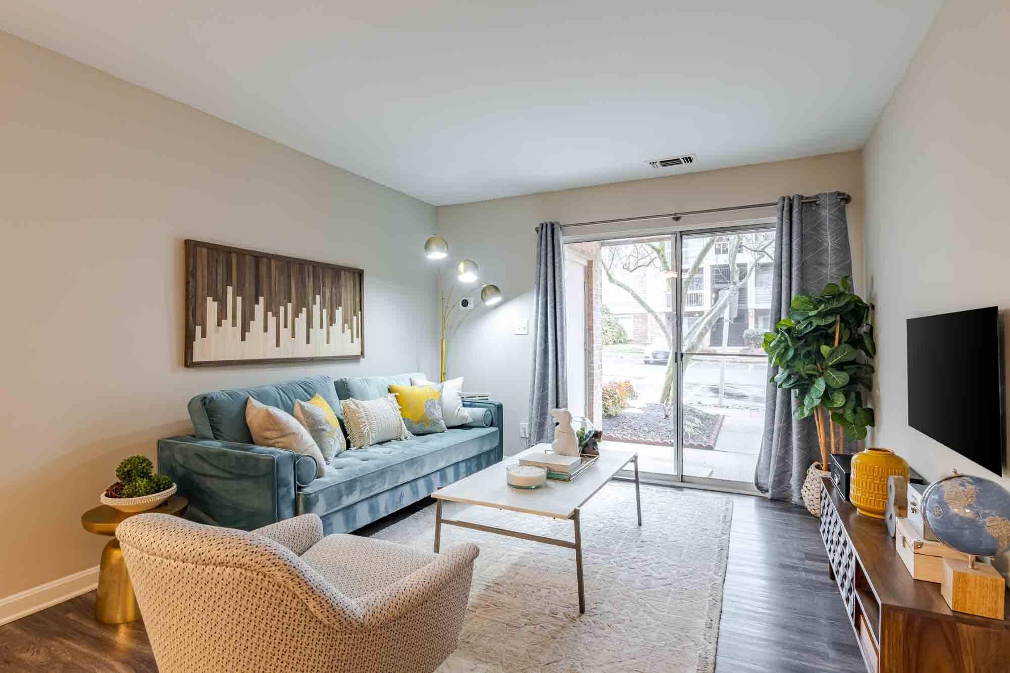 A living room with a blue couch, a chair, a coffee table, and a painting on the wall.